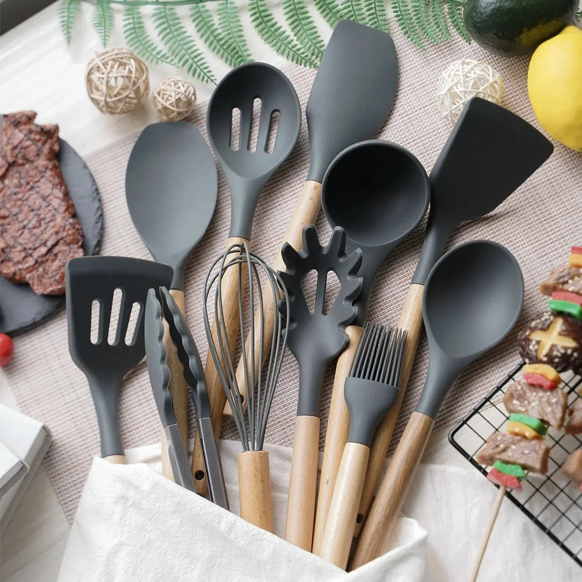 Set keukengerei van zwart siliconen met houten handvatten, uitgelegd op een tafel met citroen en knoflook