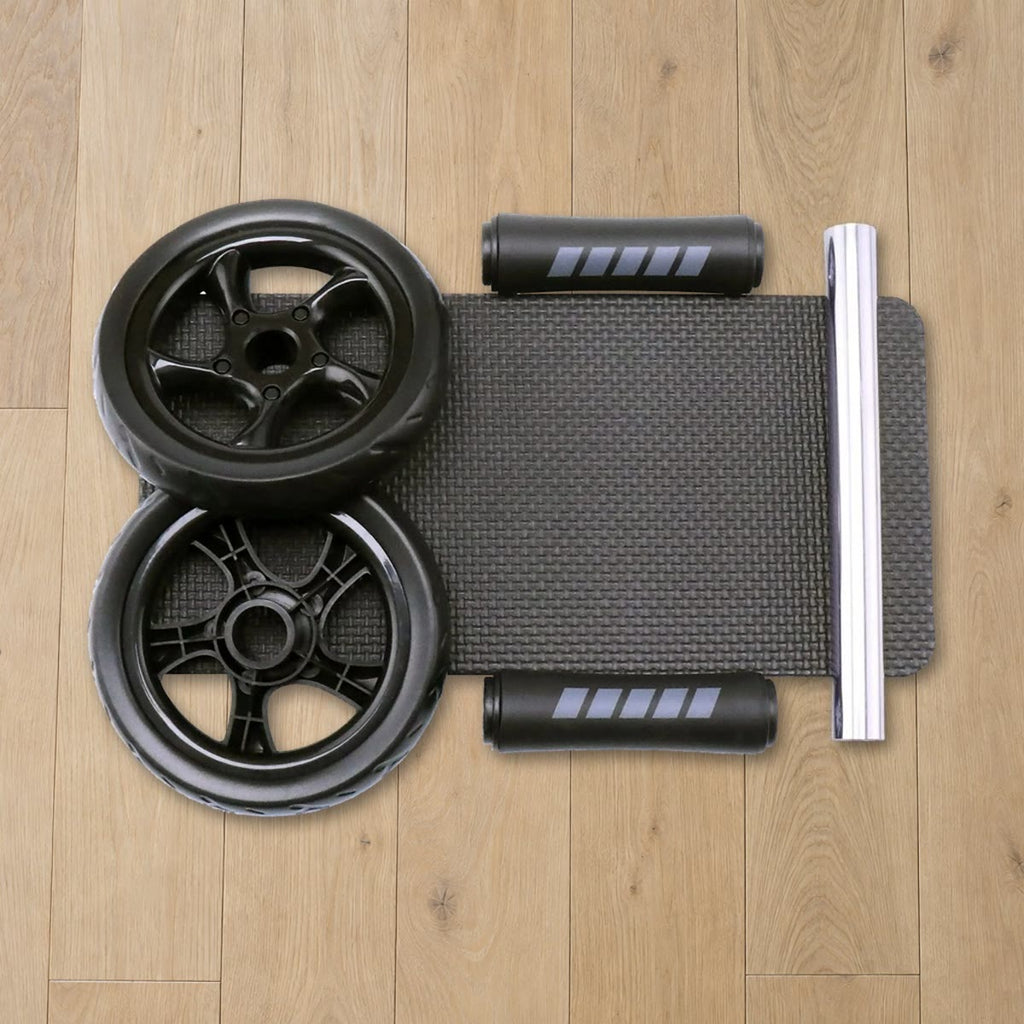 De delen van het ab wheel uitgelegd op een eikenhouten vloer: twee wielen, twee handgrepen met foam, een glanzende as en de kniemat