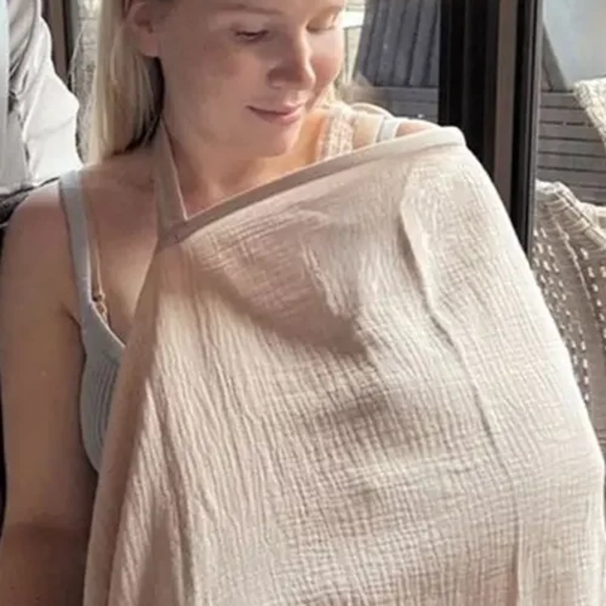 Vrouw met een kakikleurige borstvoedingsdoek over haar schouders die naar haar baby kijkt