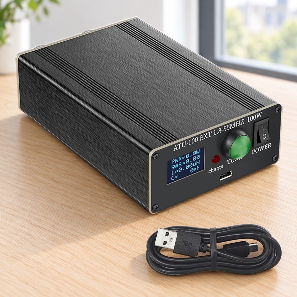 ATU-100 antennetuner met OLED-scherm, TUNE-knop en aan/uit-schakelaar op een bureau, met de meegeleverde USB-kabel