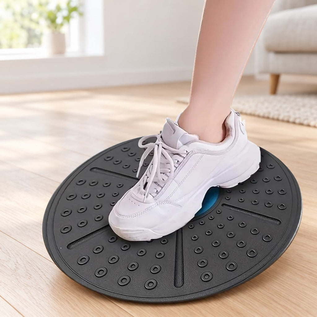 Een voet in een witte sportschoen midden op het ronde balance board, dat op een lichte houten vloer in een woonkamer ligt