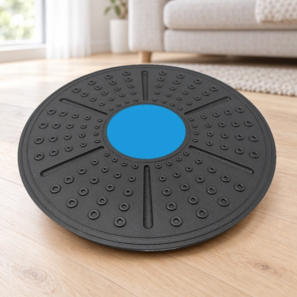 Het balance board schuin van boven gezien: zwart kunststof met noppen, zes groeven en een blauw middenvlak, op een lichte eikenhouten vloer