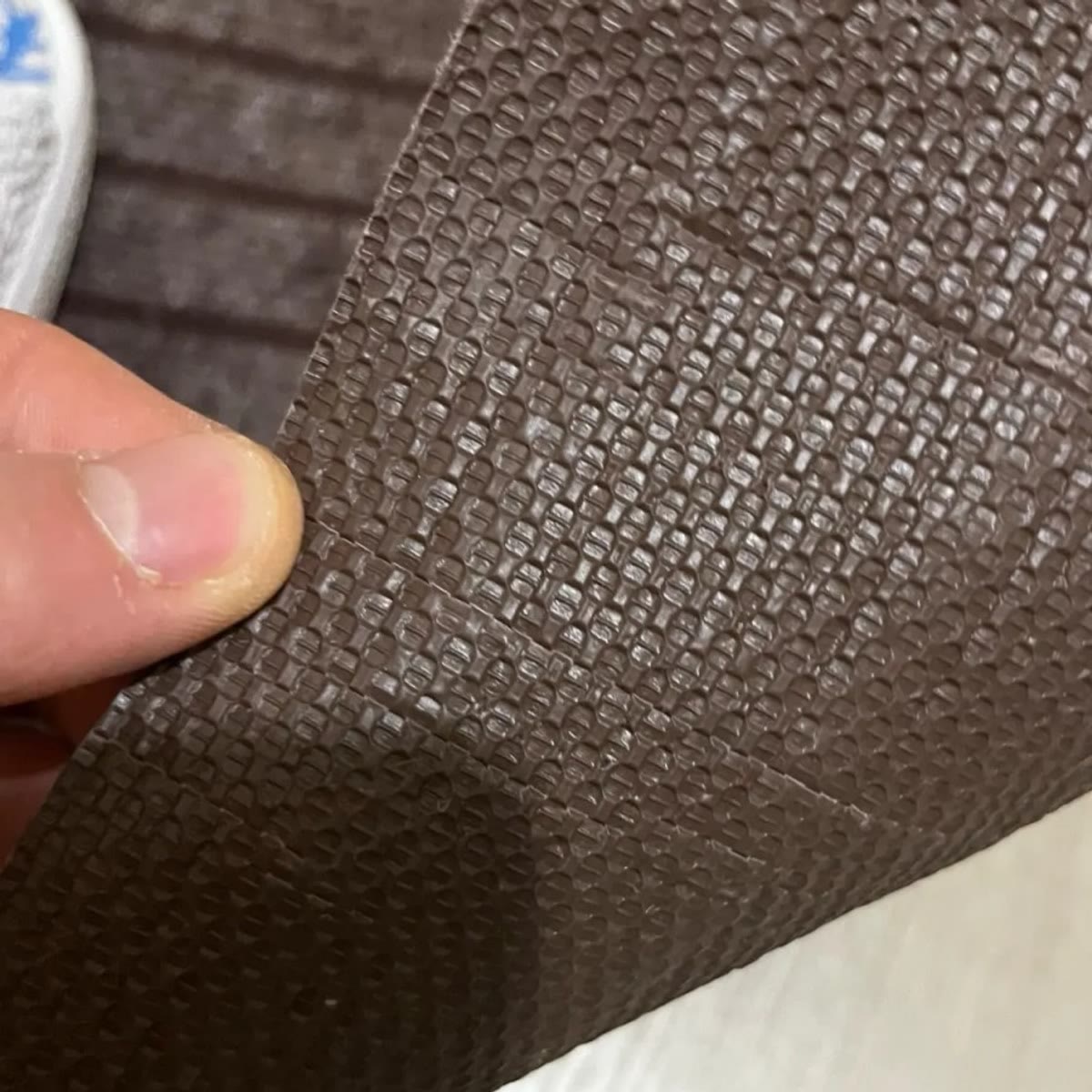De onderkant van de deurmat: bruin rubber met ruitpatroon, omhooggehouden met een vinger