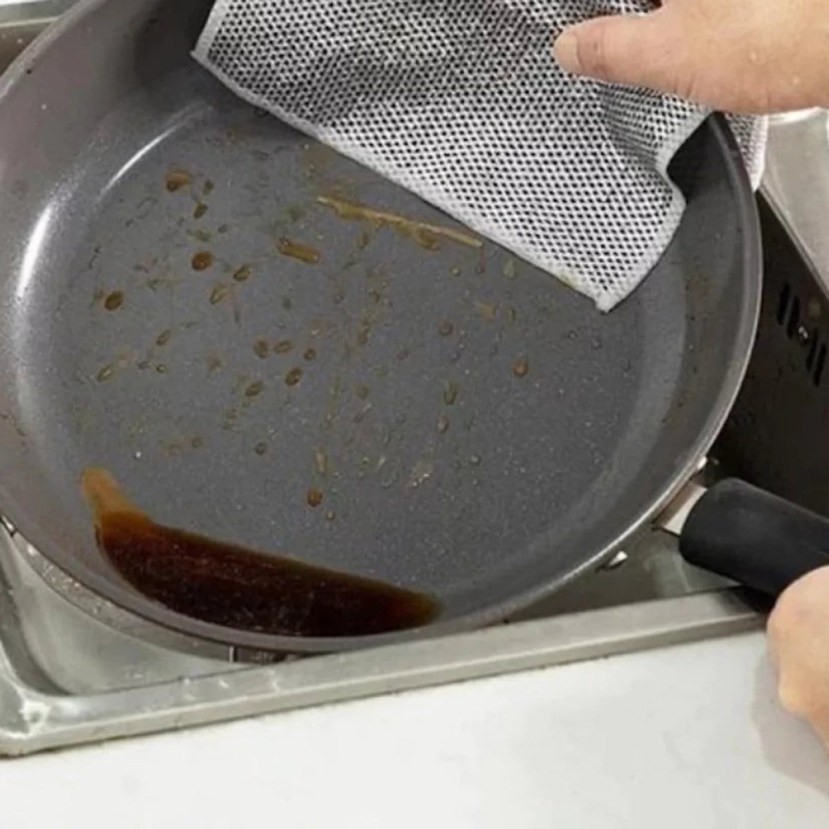 Draadvaatdoekje in een koekenpan met aangekoekte vlekken, boven de gootsteen