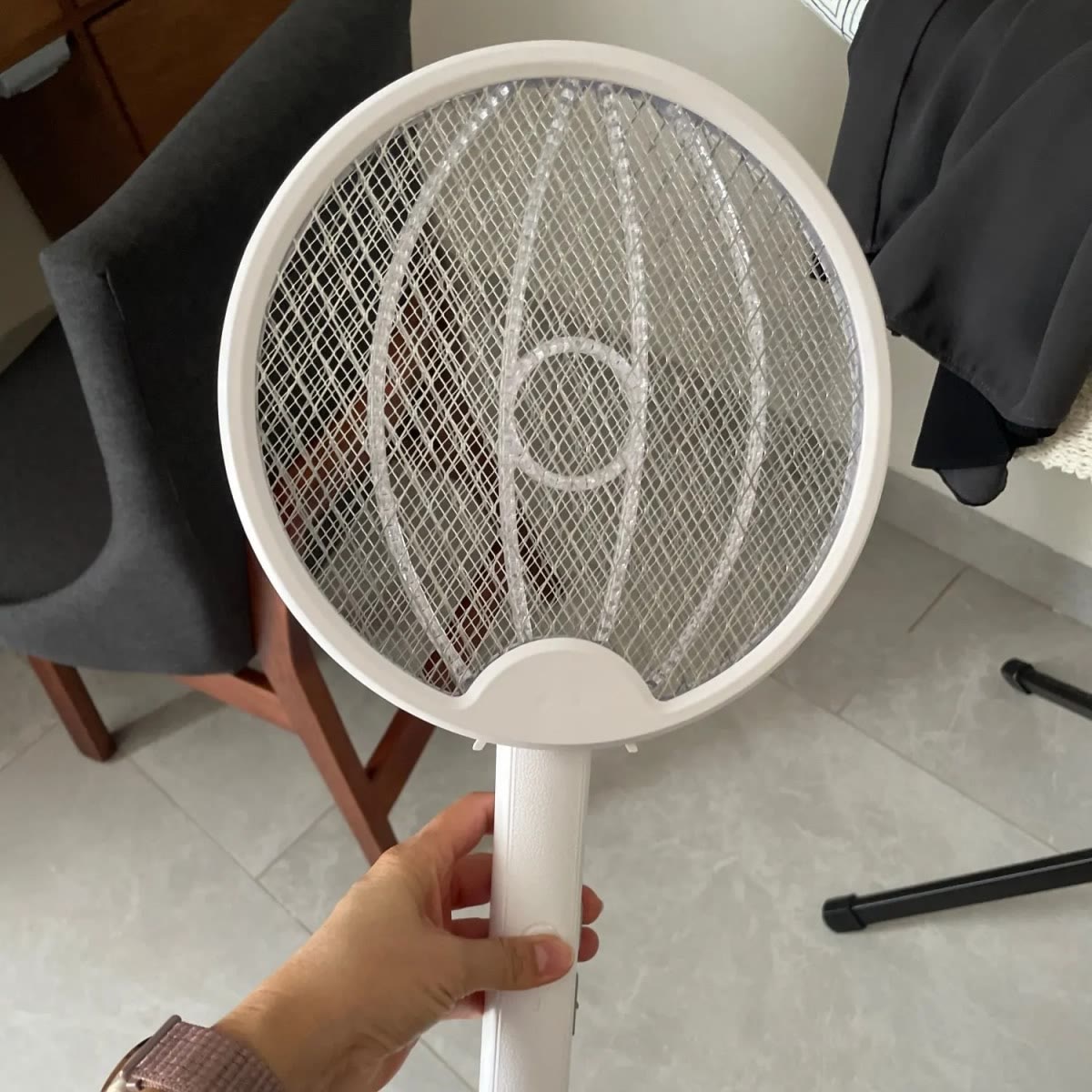 Hand die de vliegenmepper bij de steel vasthoudt met het ronde net omhoog, in een kamer met tegelvloer