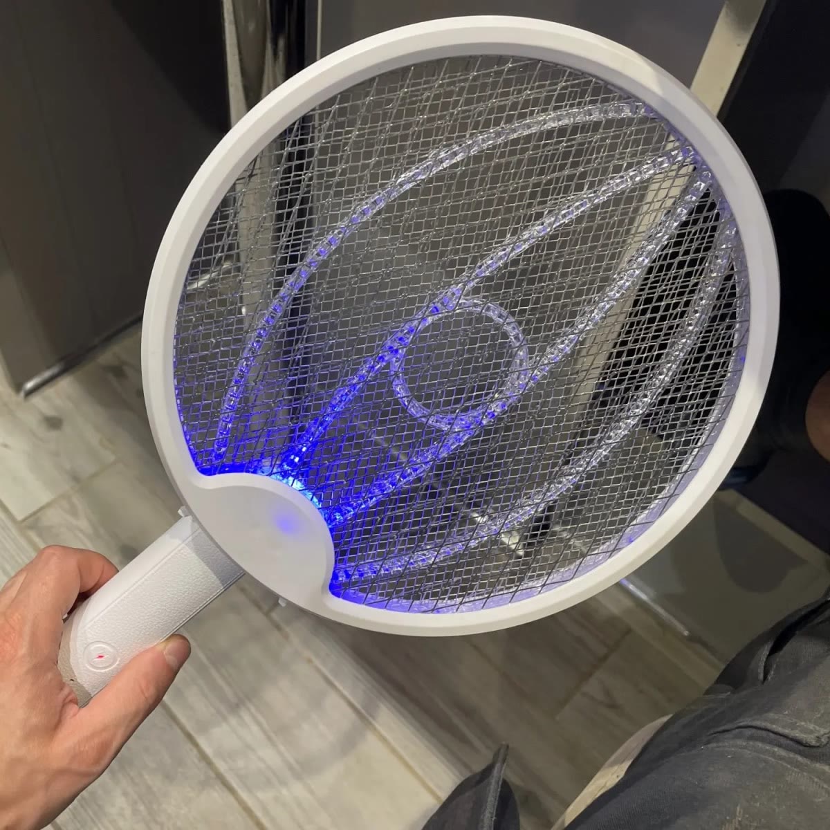 De vliegenmepper in de hand, met de steel in een hoek en de blauwe leds aan langs de bogen in het net