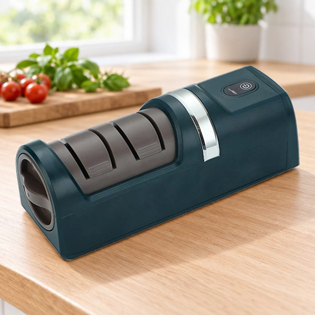 Donkergroene elektrische messenslijper op een eiken aanrecht, met tomaten en basilicum op de achtergrond