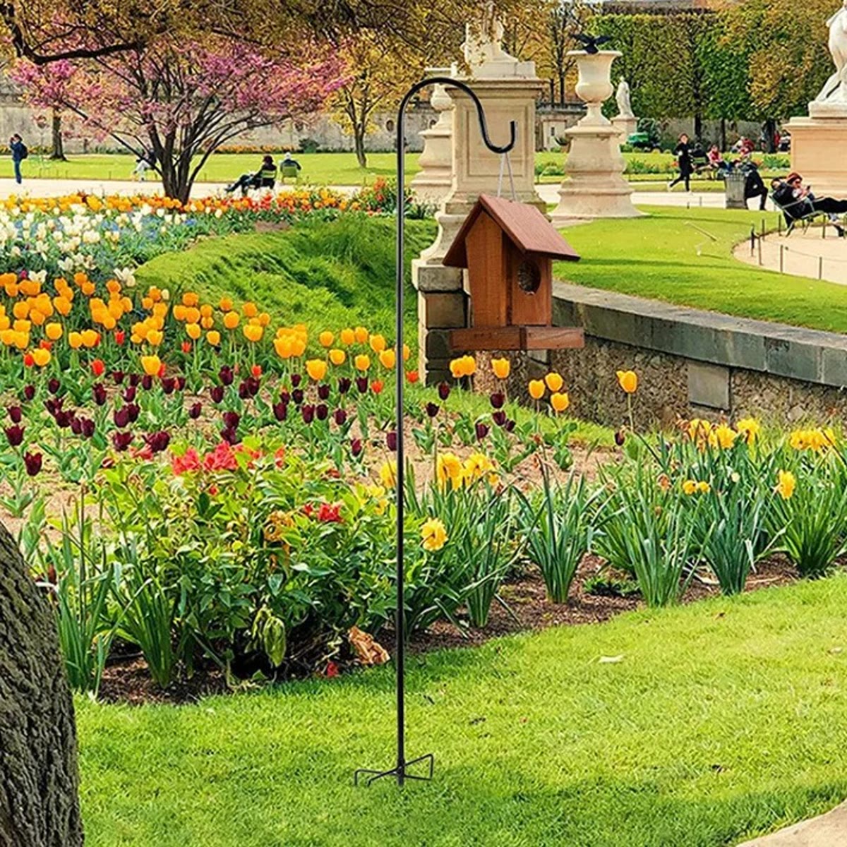 Zwarte haak in een border met tulpen, met een klein houten vogelhuisje aan de haak
