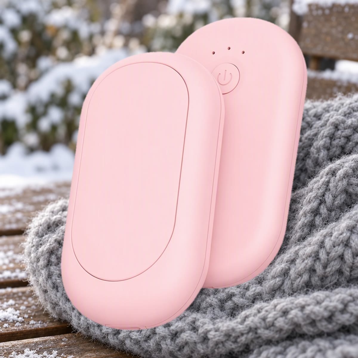 Roze oplaadbare handwarmer in twee helften op een grijze wollen sjaal buiten in de sneeuw