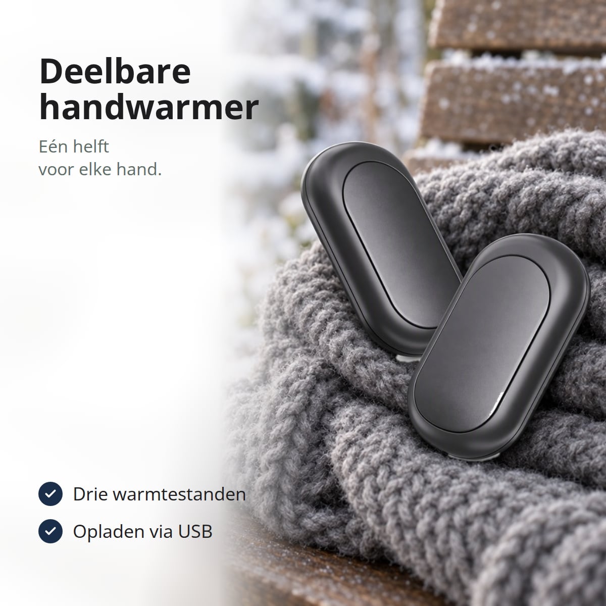 Zwarte oplaadbare handwarmer in twee helften op een wollen sjaal op een bankje in de sneeuw