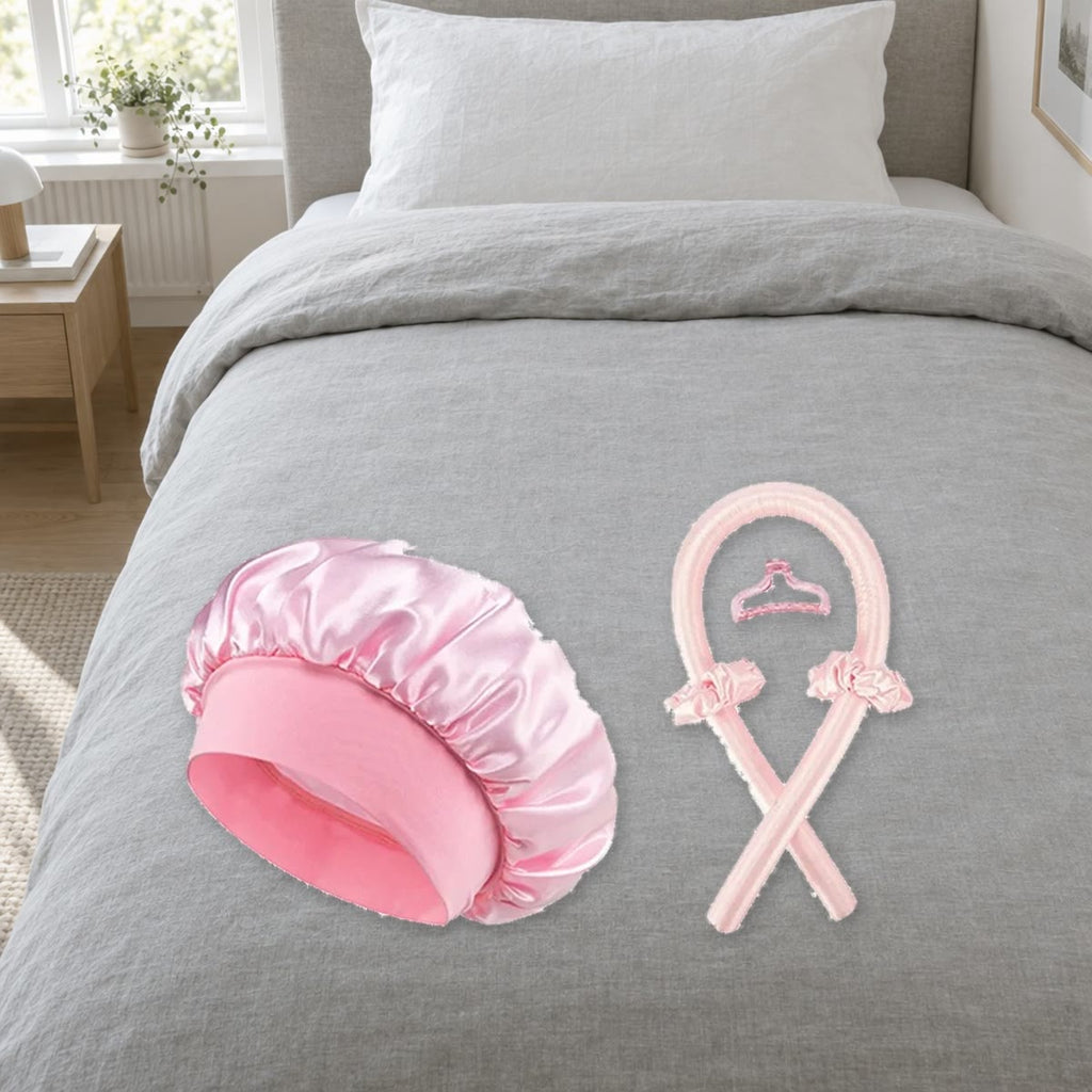 Heatless curls set in roze: krulstaaf, satijnen muts, twee scrunchies en haarklem op grijs beddengoed