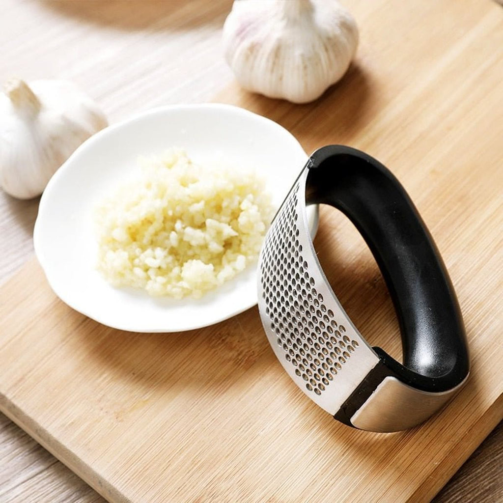 De knoflookpers op een plank naast een schaaltje geperste knoflook