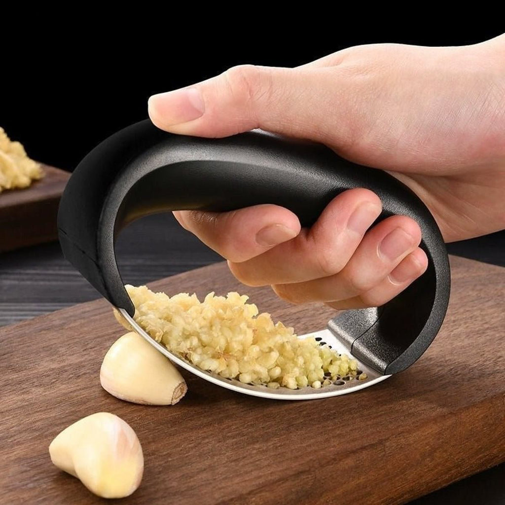 Hand rolt de knoflookpers over knoflookteentjes op een donkere houten plank