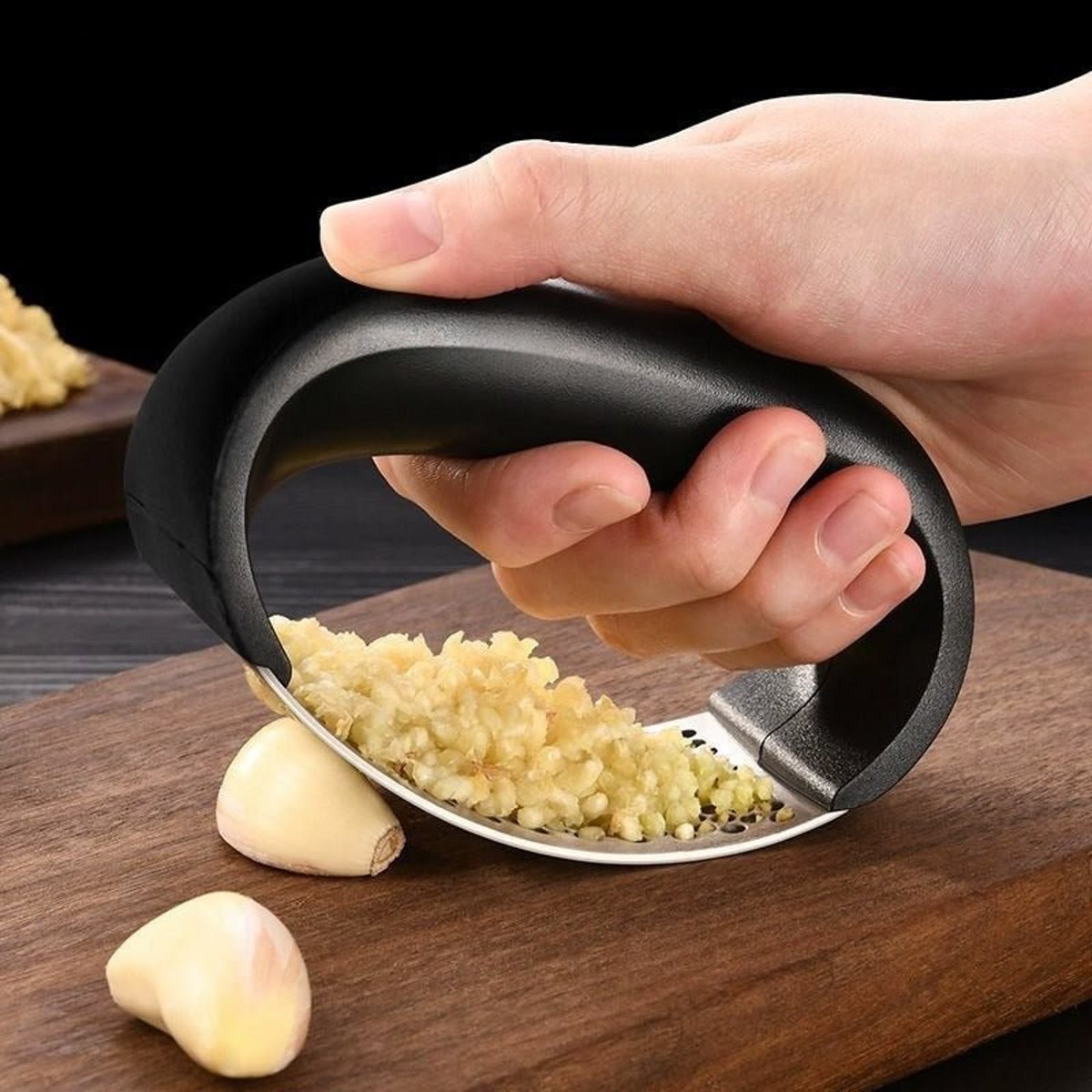 Hand rolt de knoflookpers over knoflookteentjes op een donkere houten plank