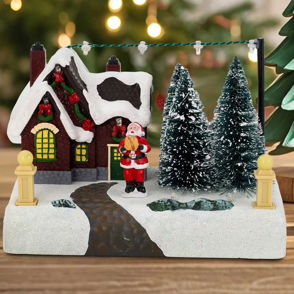 Het kerstdorp uit bij daglicht voor een kerstboom, het huisje met sneeuwdak en de kerstman bij de deur