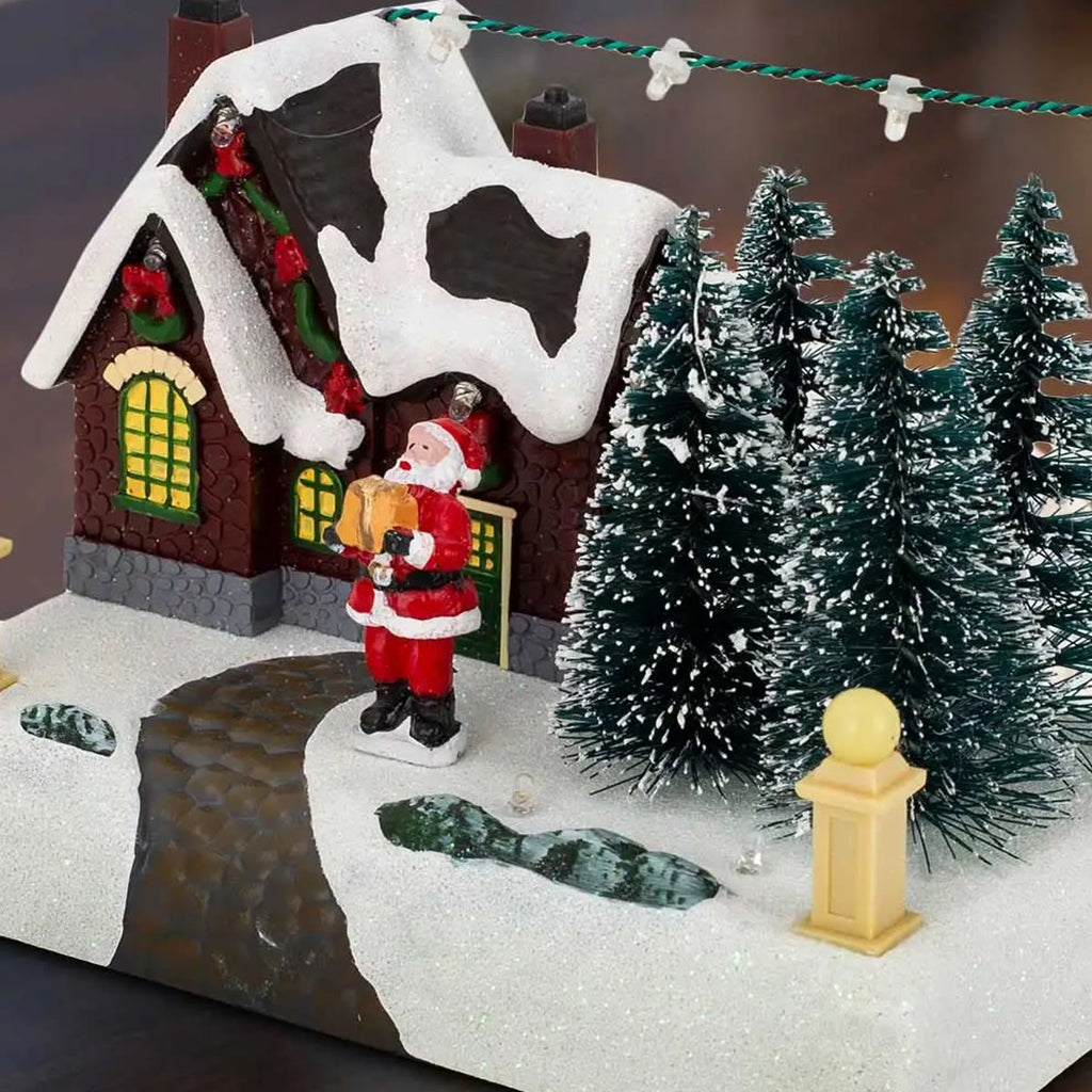 Het kerstdorp schuin van voren gezien op een donkere tafel, het lichtsnoer van de schoorsteen naar de paal