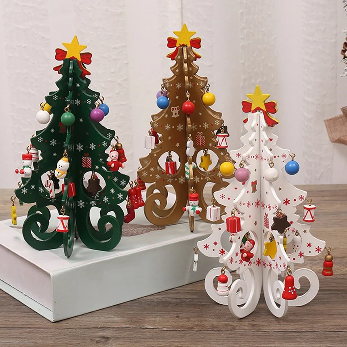 Drie kleine houten kerstboompjes, groen, goud en wit, met kleine houten versieringen, ster en strik