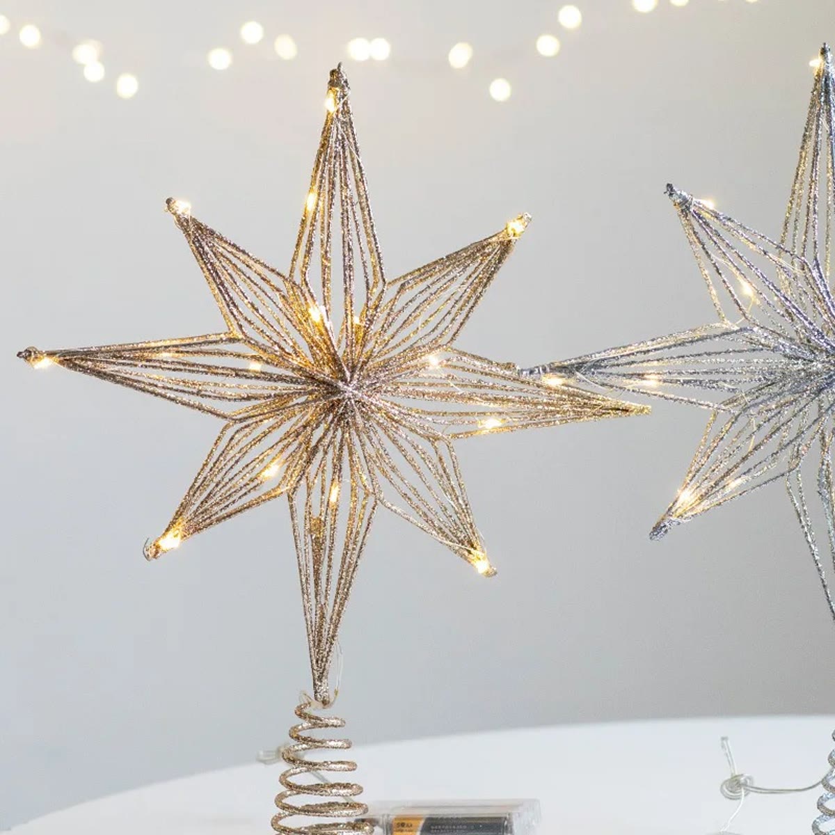 Gouden kerstboomster met brandende ledlampjes, 8-puntige ster van metaaldraad op een witte tafel