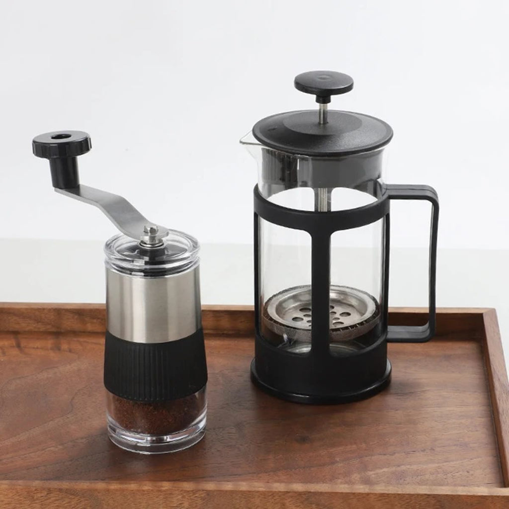 Handmatige koffiemolen met gemalen koffie naast een cafetière op een houten plank