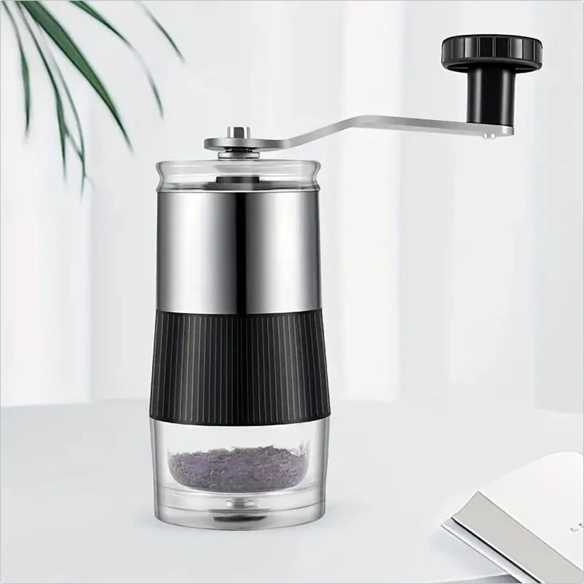 De koffiemolen van roestvrij staal met slinger voor een lichte muur met een groene plant