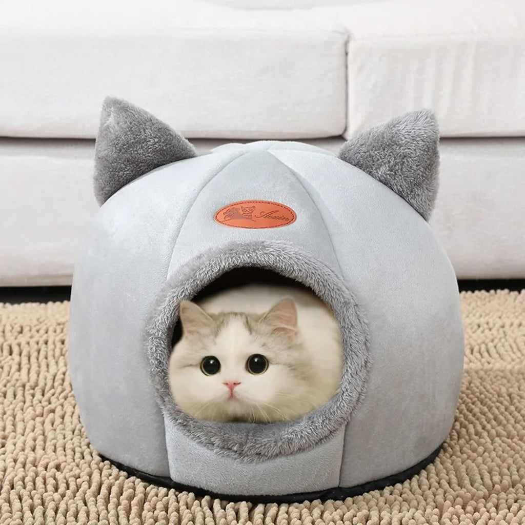 Kat die uit een lichtgrijs kattenhol met oortjes kijkt, op een beige kleed