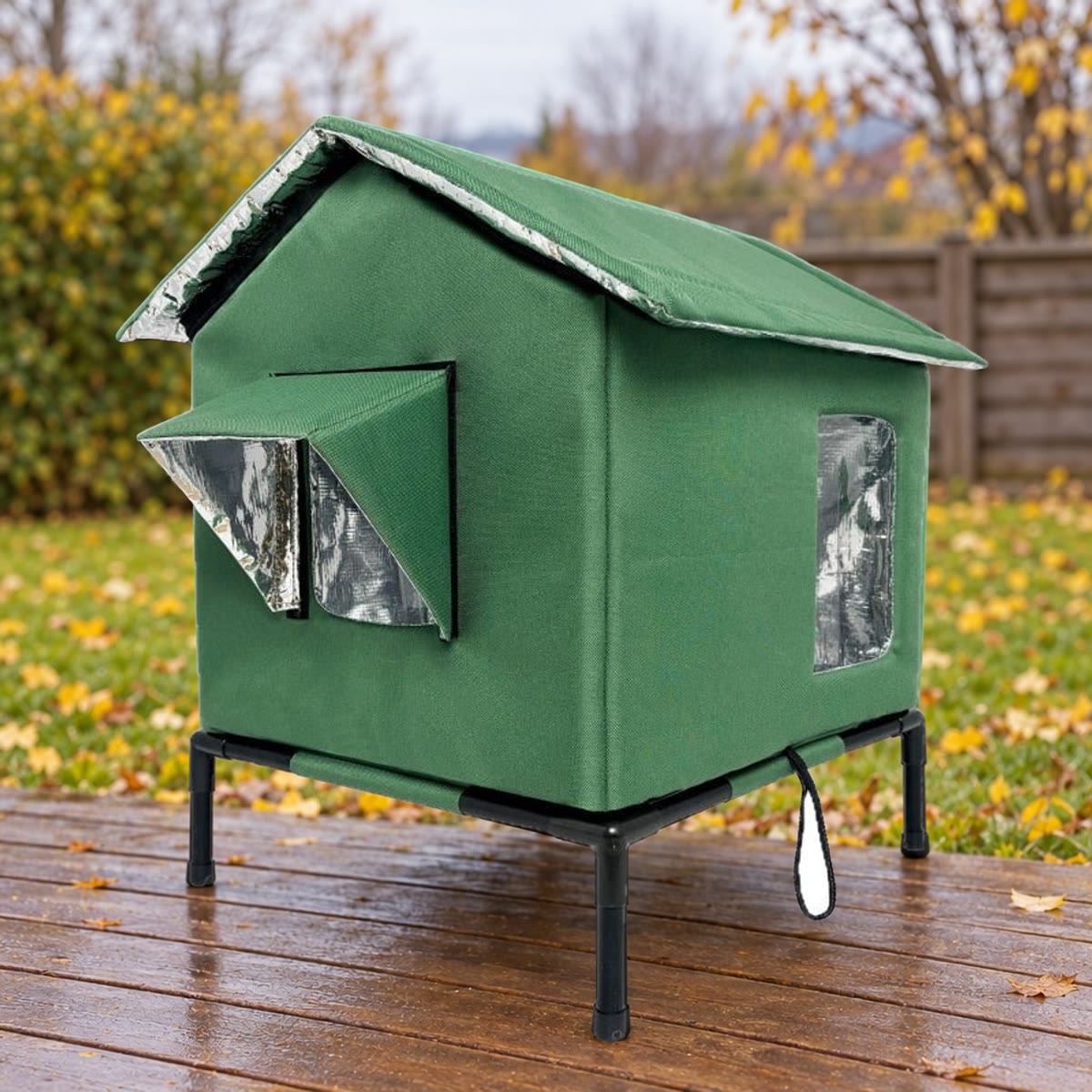 Donkergroen kattenhuis op een standaard op een terras, met gazon en herfstbladeren op de achtergrond