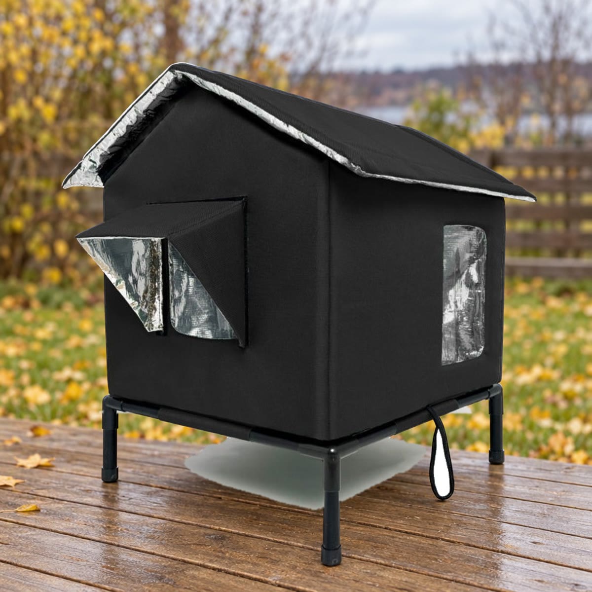 Zwart kattenhuis op een standaard op een terras, met gazon en herfstbladeren op de achtergrond