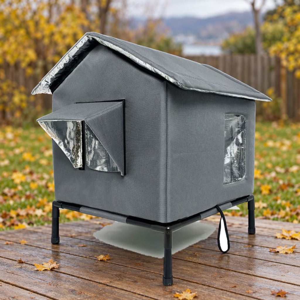 Donkergrijs kattenhuis op een standaard op een terras, met gazon en herfstbladeren op de achtergrond