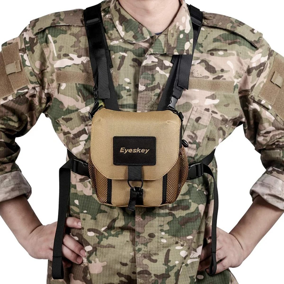 Het verrekijker harnas gedragen op de borst over een camouflagejas, met zandkleurige tas en zwarte banden over de schouders
