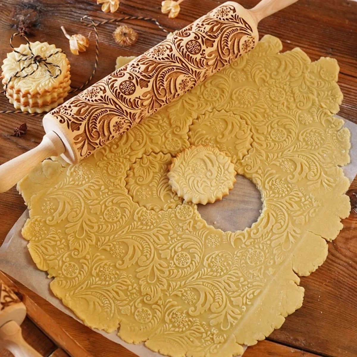 Deegroller met bloemenpatroon op uitgerold koekdeeg met ingedrukt patroon en uitgestoken koekjes