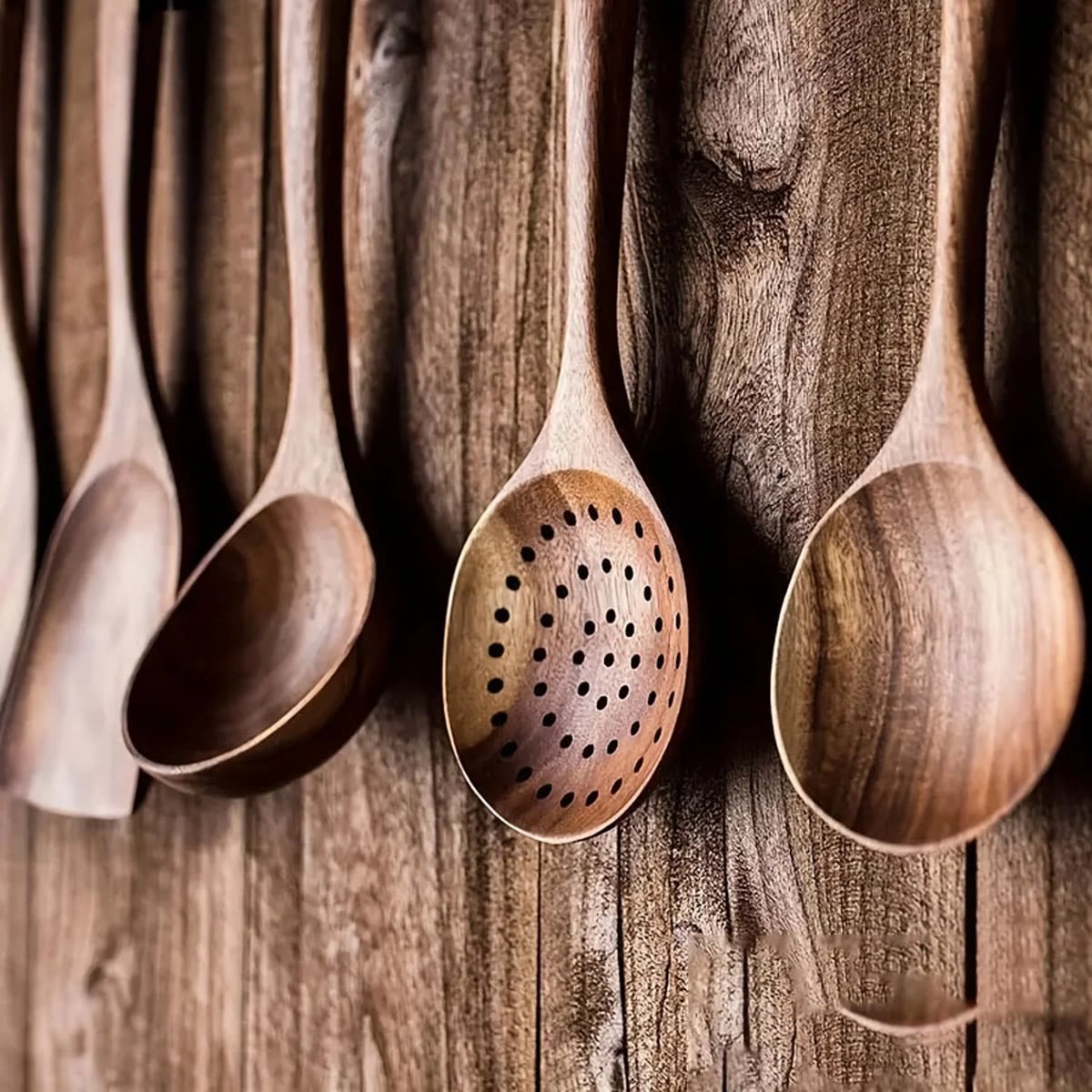 Pollepels en schuimspaan van teak, opgehangen aan een wand van donker hout