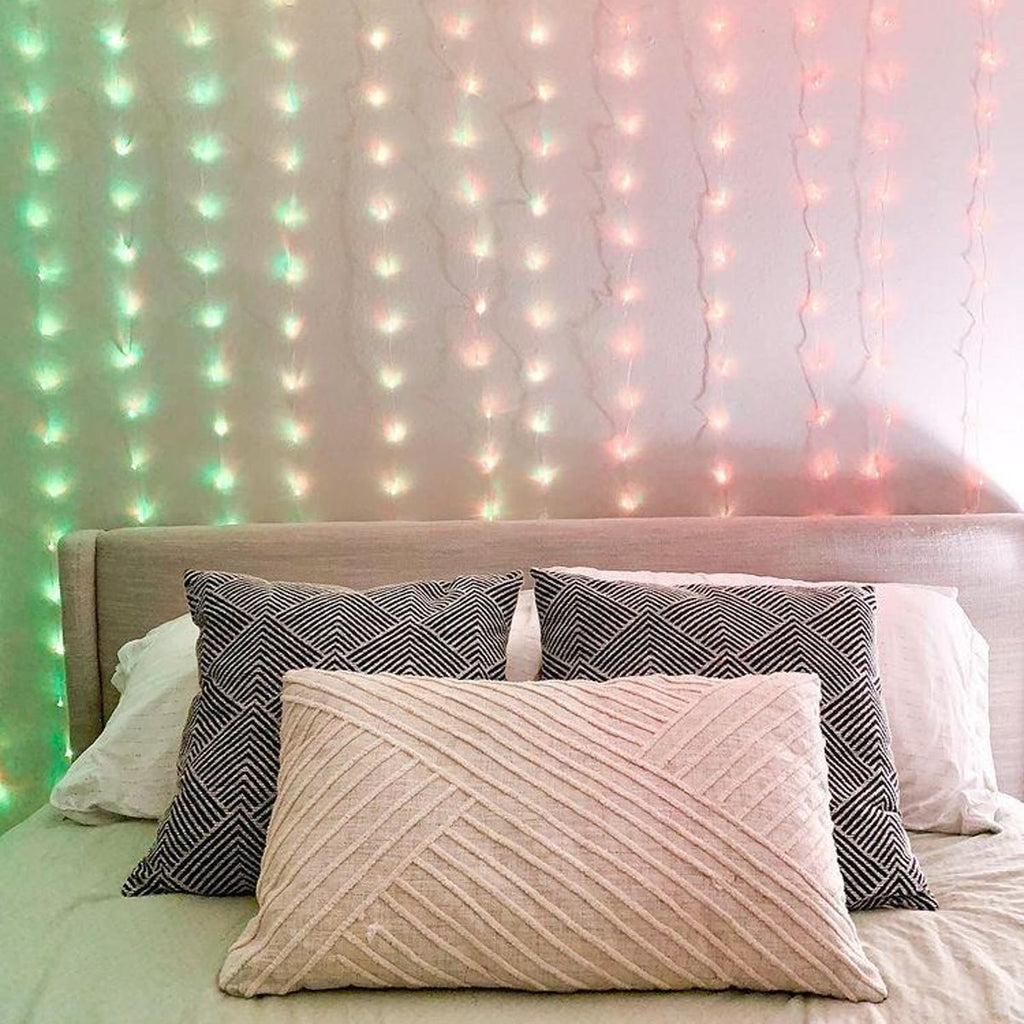 Meerkleurig lichtgordijn dat groen, roze en blauw oplicht aan de muur achter een bed