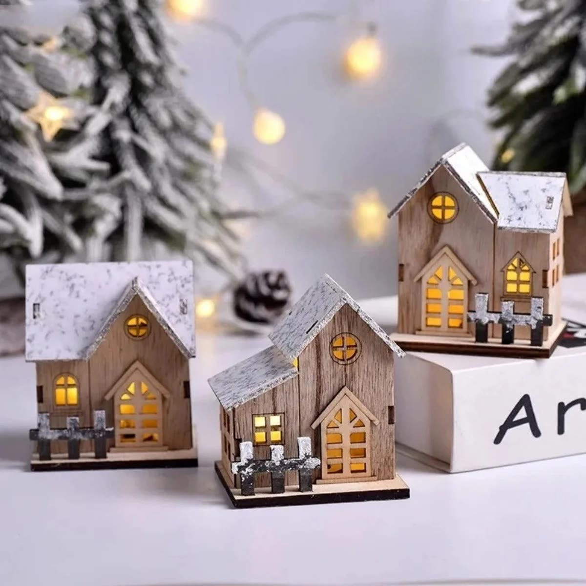 De drie kersthuisjes uit de set met het licht aan, met kerstlichtjes op de achtergrond