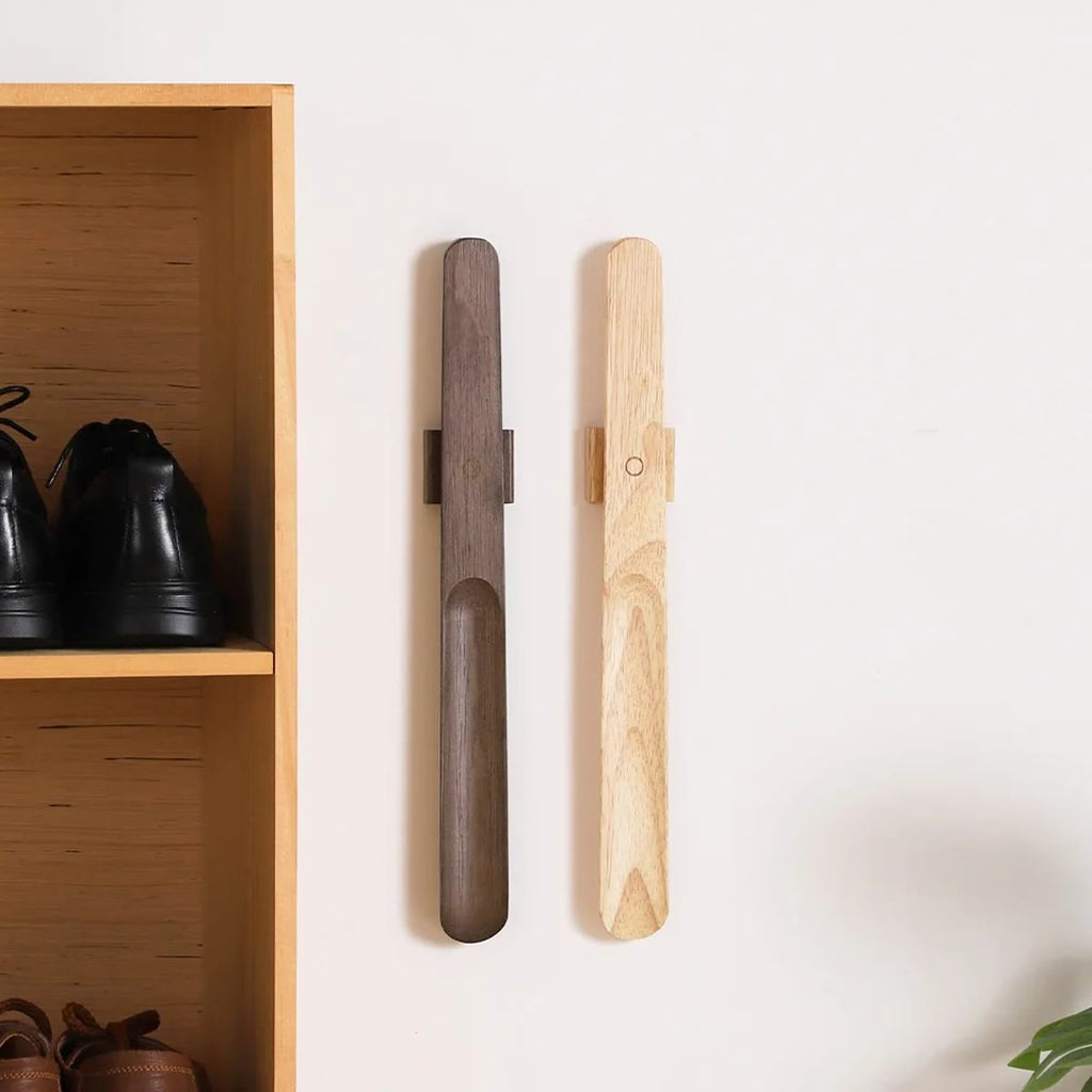 Twee houten schoenlepels met magneet, een donkerbruine en een lichte, opgehangen aan hun wandhouders naast een schoenenrek