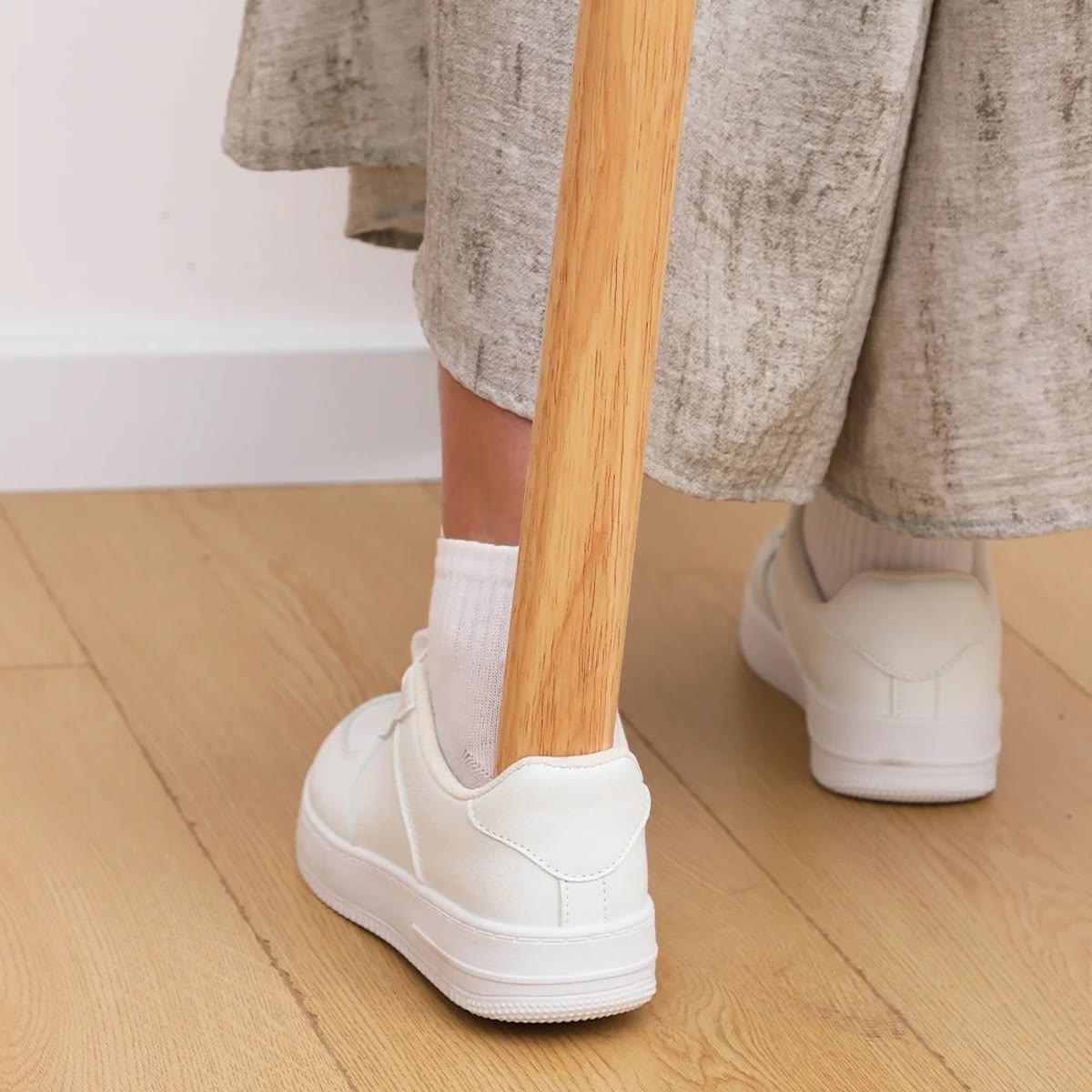 De lichte schoenlepel in gebruik achter de hiel van een witte sneaker op een lichte houten vloer