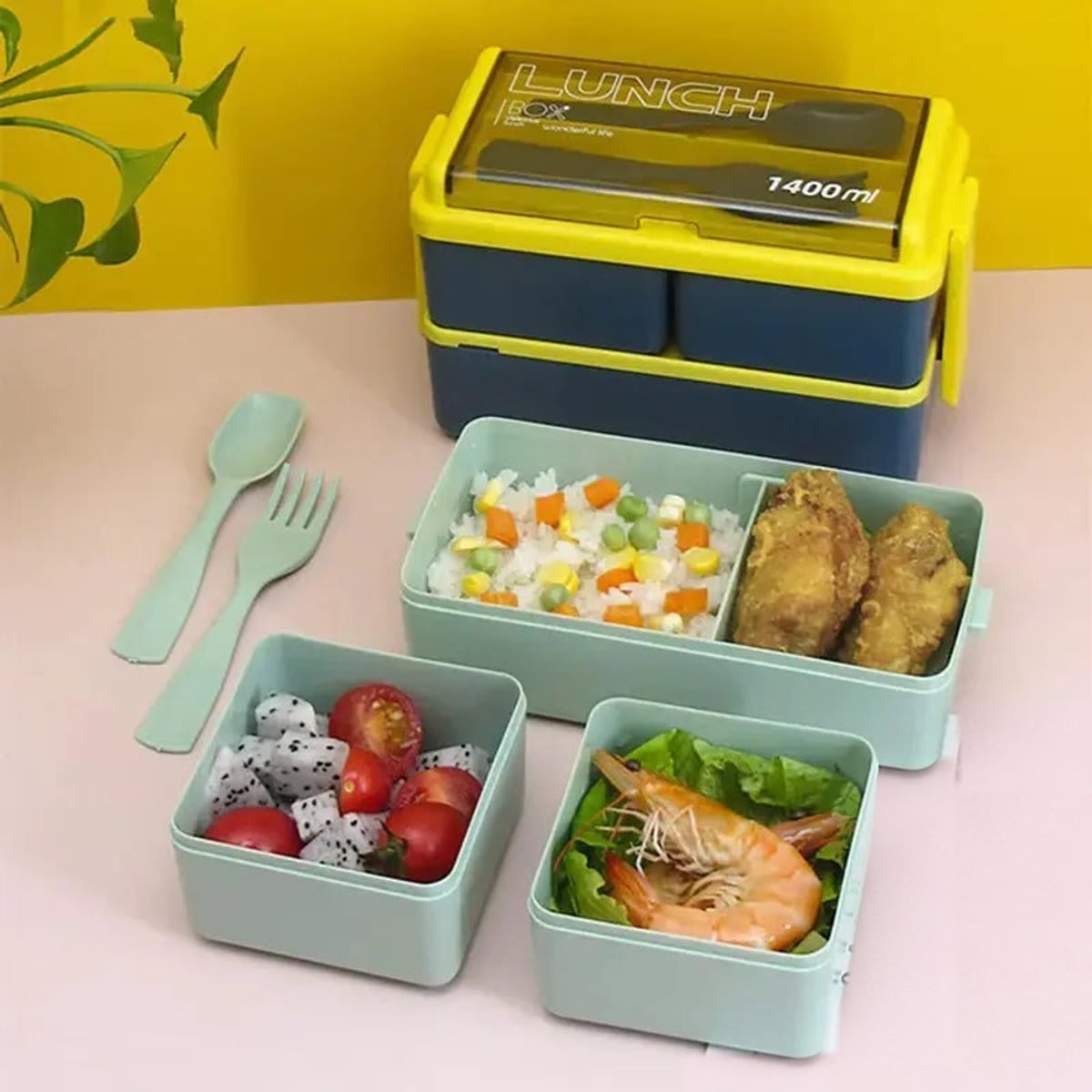 Groene bento box open: rijst en kip in de onderste bak, fruit en salade in de twee kleine bakjes, lepel en vork ernaast