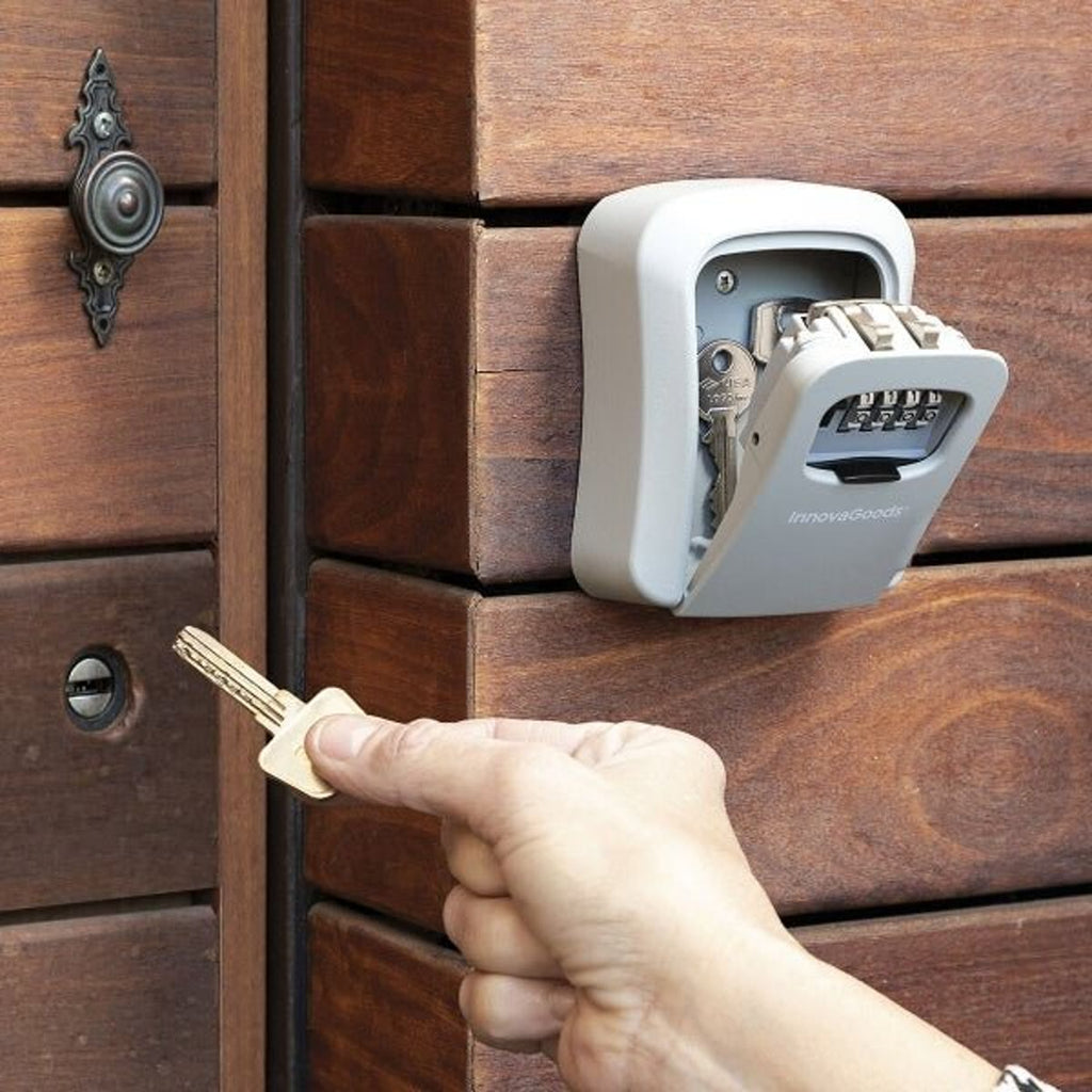 Hand die een sleutel uit een open sleutelkluis aan een houten muur pakt