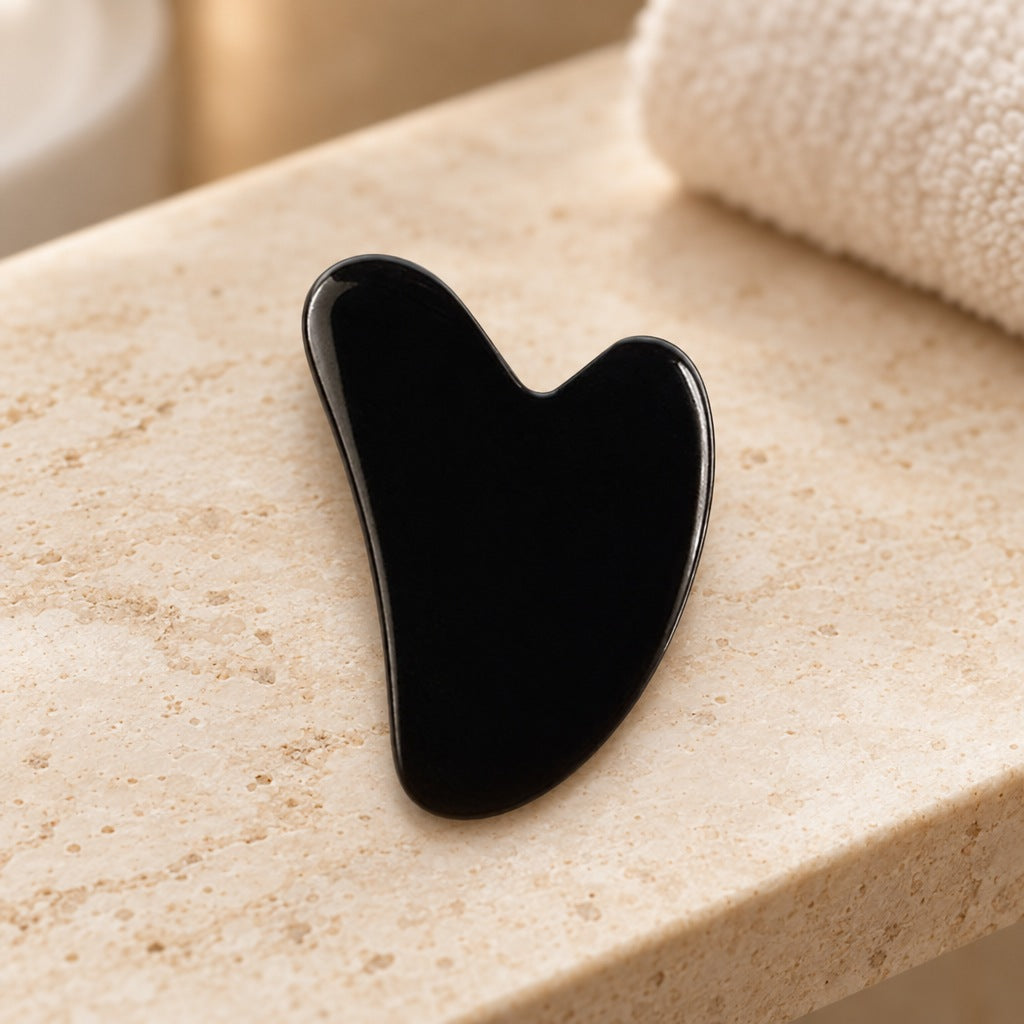 Hartvormige gua sha van zwarte obsidiaan op een travertin plank in de badkamer