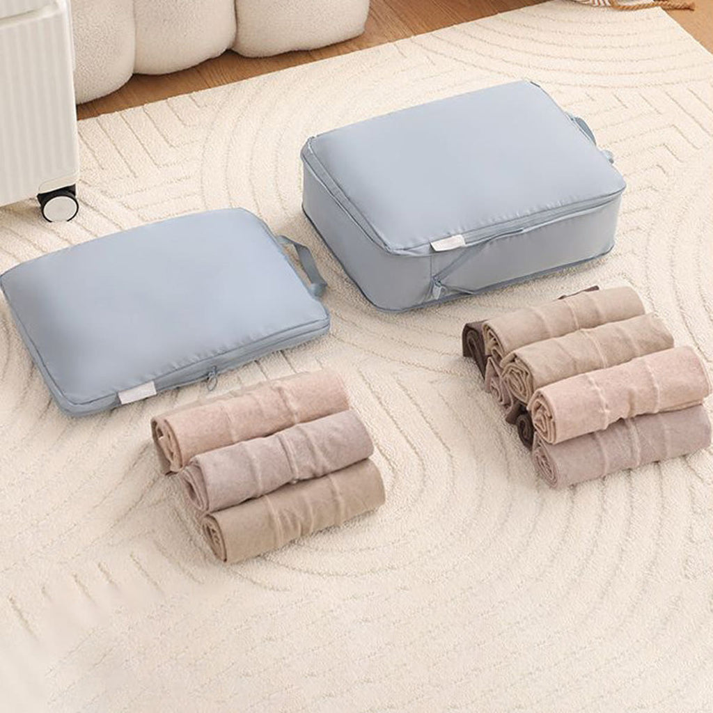 Grijze packing cubes naast opgerolde truien en T-shirts, klaar om in de tassen te gaan