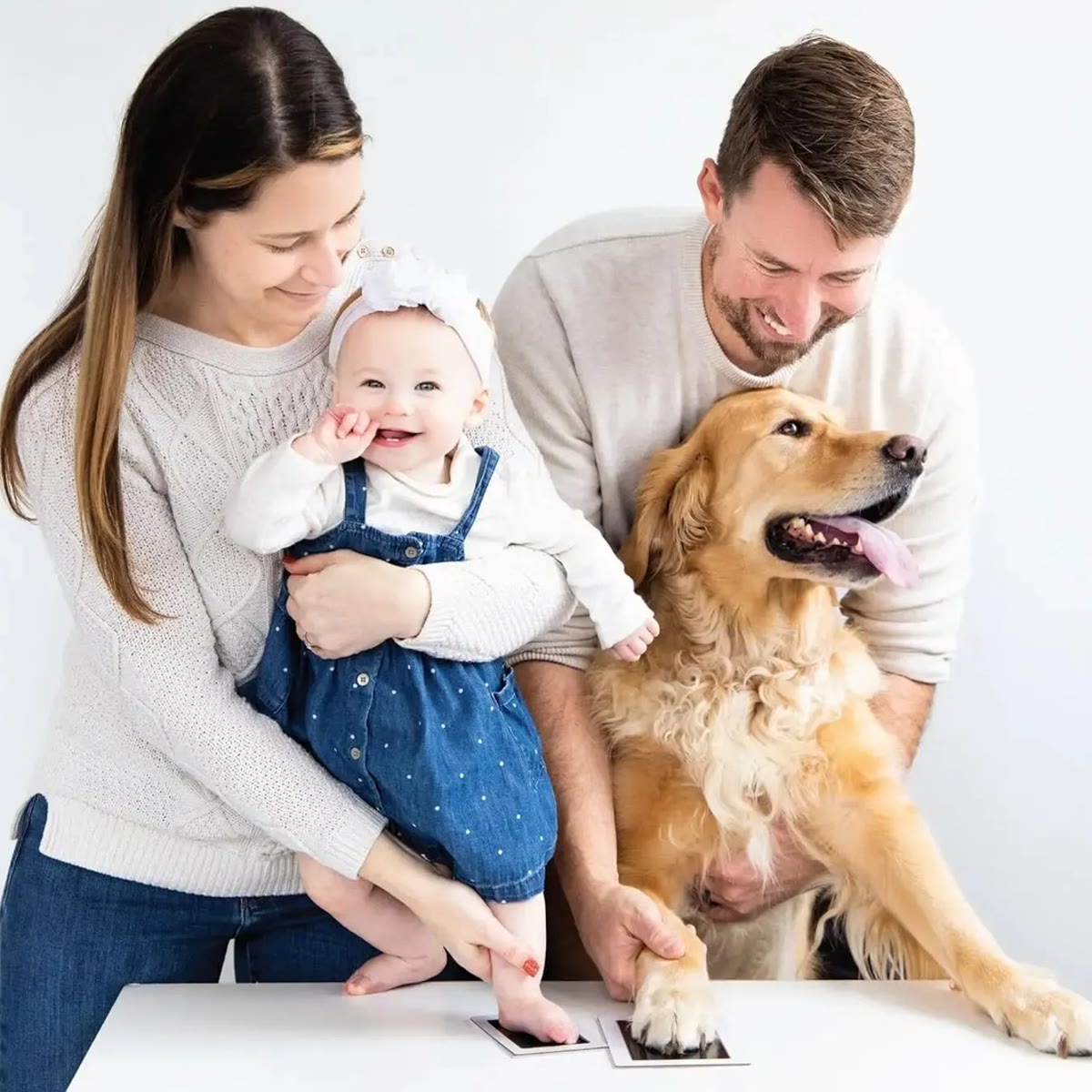 Gezin met een baby en een golden retriever dat een afdruk van een hand en een poot maakt
