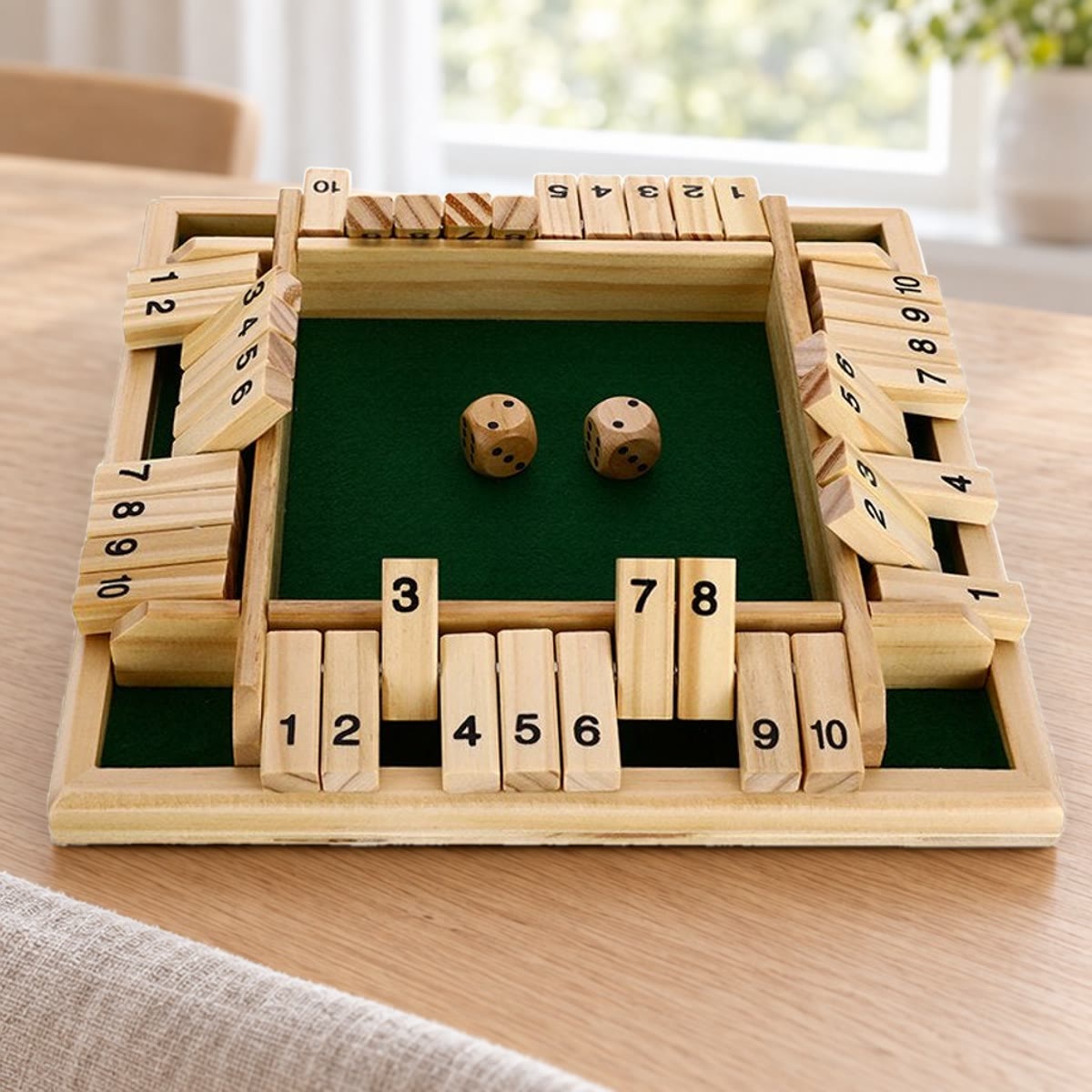 Shut the Box dobbelspel van hout met twee dobbelstenen op groen vilt, op een lichte eikenhouten tafel in een woonkamer