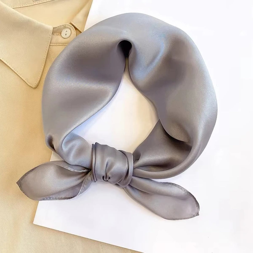 Kleine grijze zijden sjaal met een strik geknoopt, op wit papier naast een lichte blouse