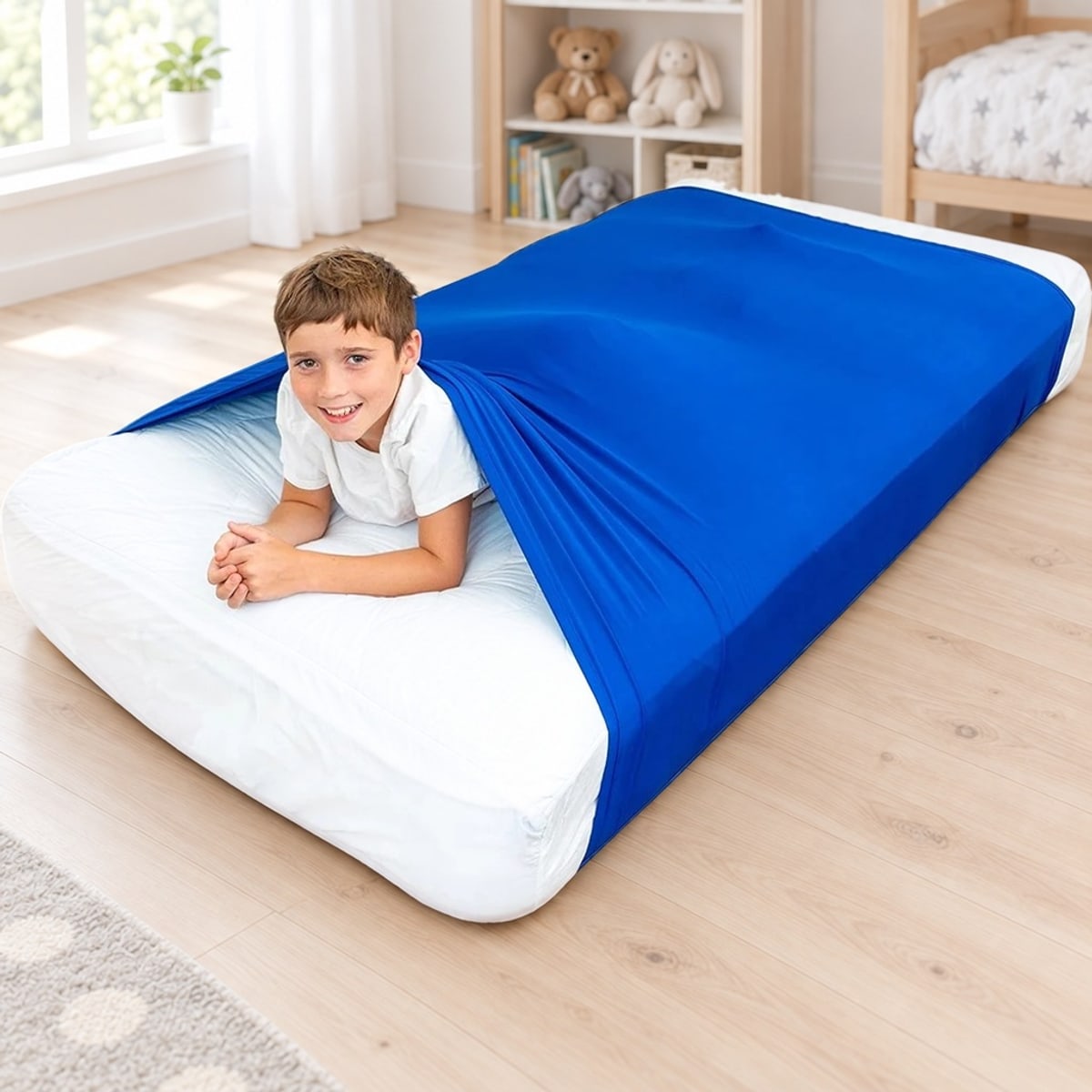 Jongen kruipt onder een blauwe slaaptunnel om het matras, in een lichte kinderkamer