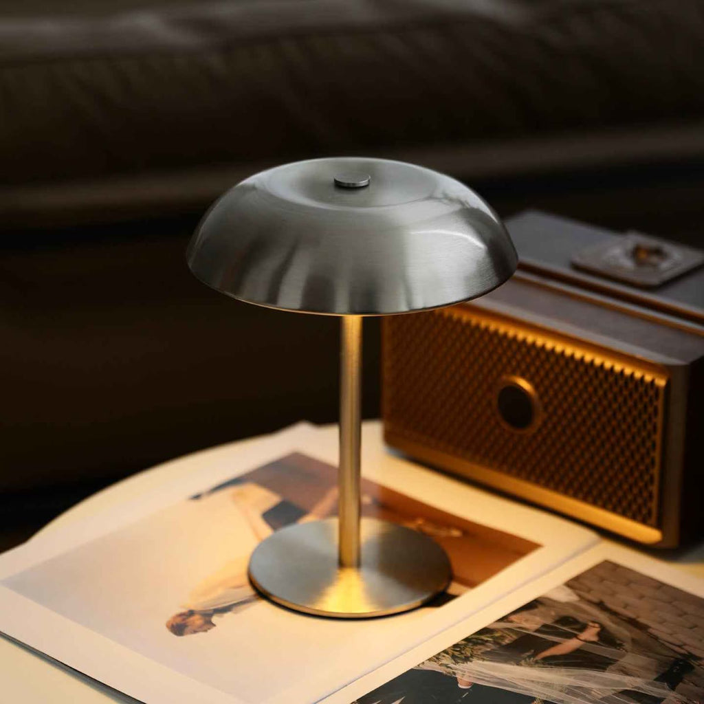Mushroom lamp van geborsteld metaal, aan op een tafel naast een oude radio en oude foto's
