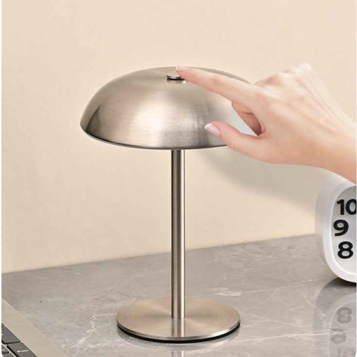 Een hand die op de touch-sensor bovenop de mushroom lamp drukt, op een marmeren blad