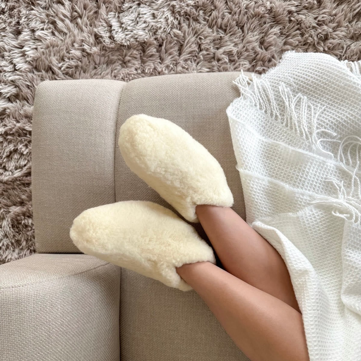 Witte wollen pantoffels op een bank met een plaid over de benen
