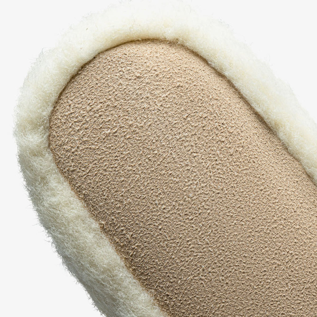 Close-up van de leren zool onder de witte wollen pantoffel