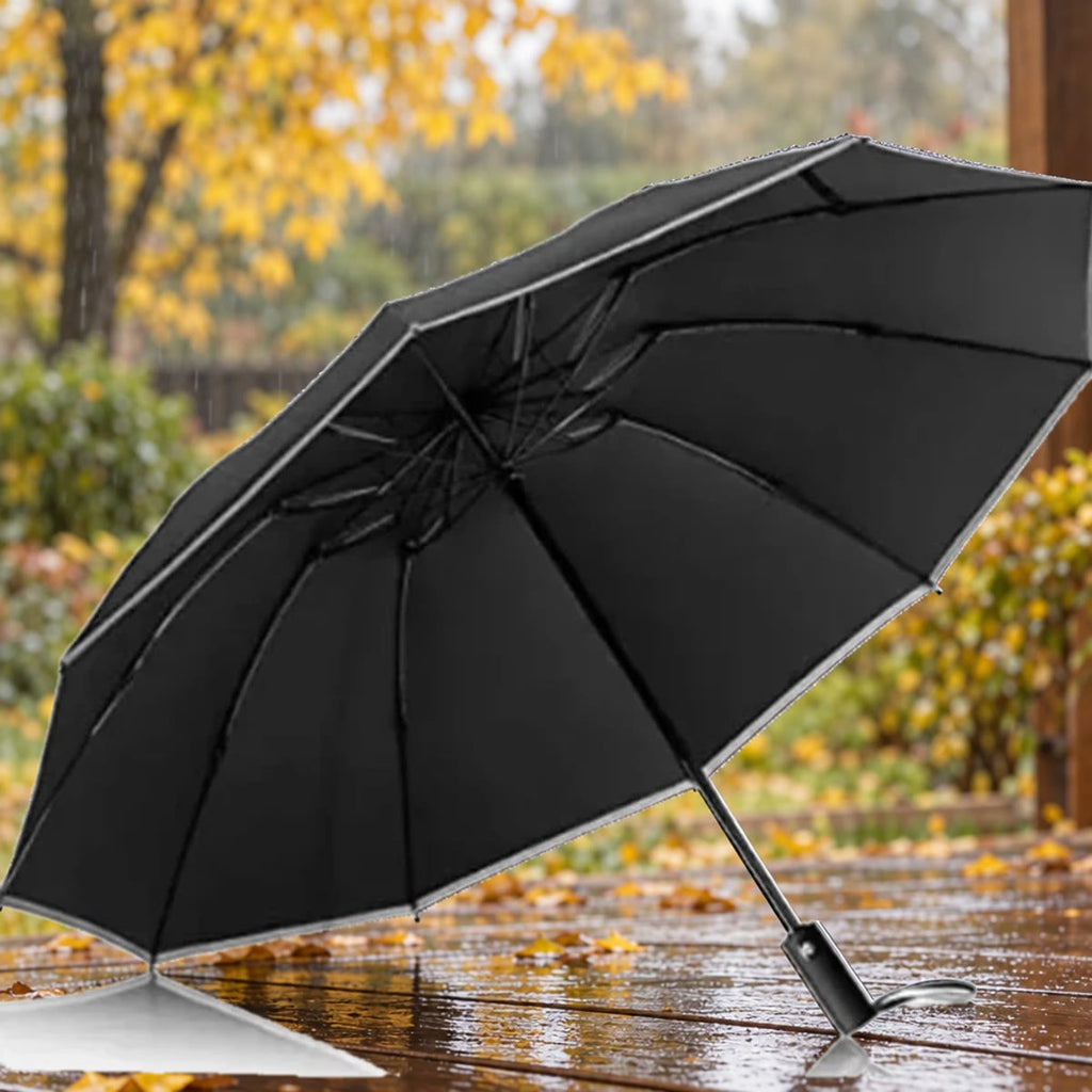 Open zwarte stormparaplu met reflectie langs de rand op een nat terras met herfstbladeren