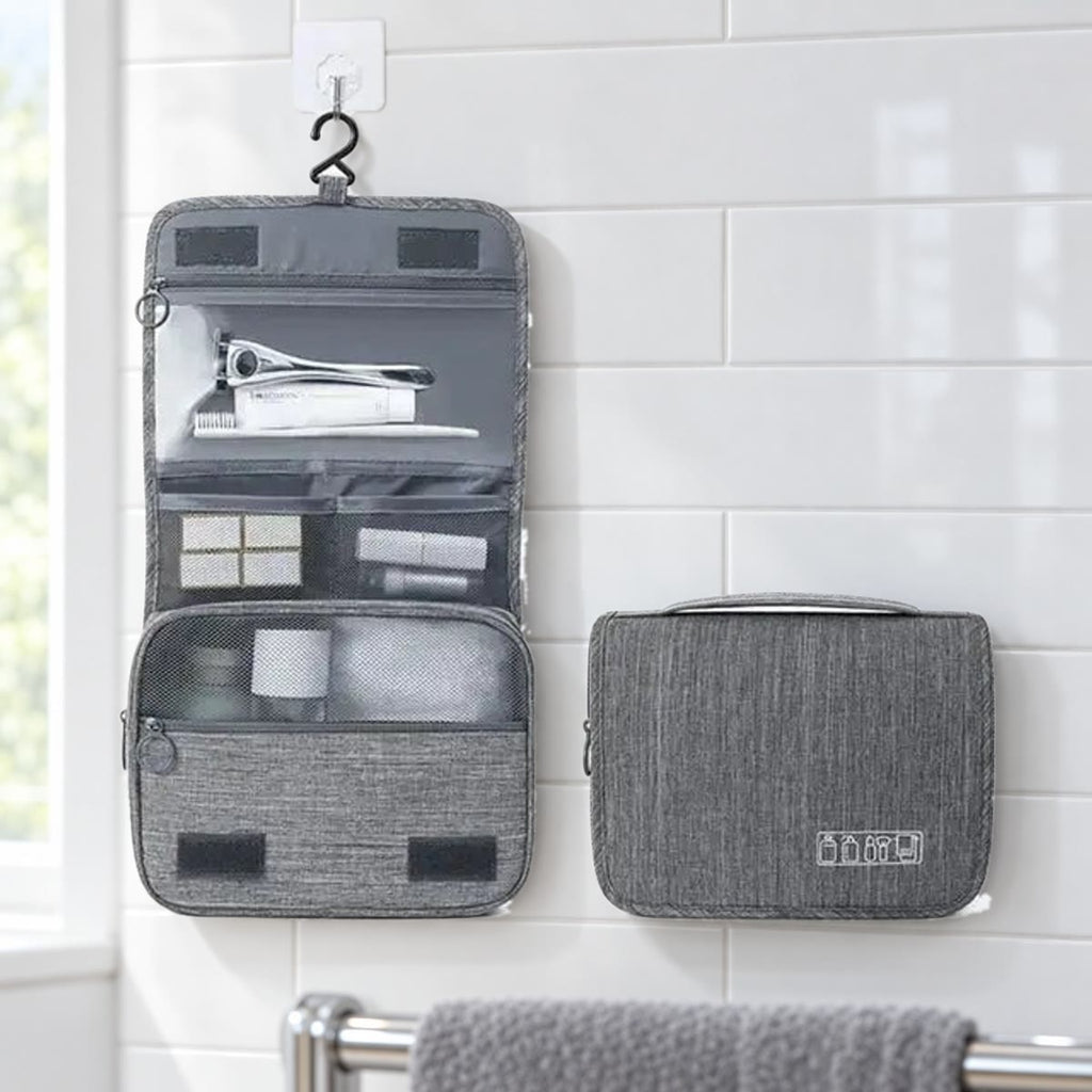 Grijze hangende toilettas, uitgevouwen en dicht, tegen een witte tegelwand in de badkamer