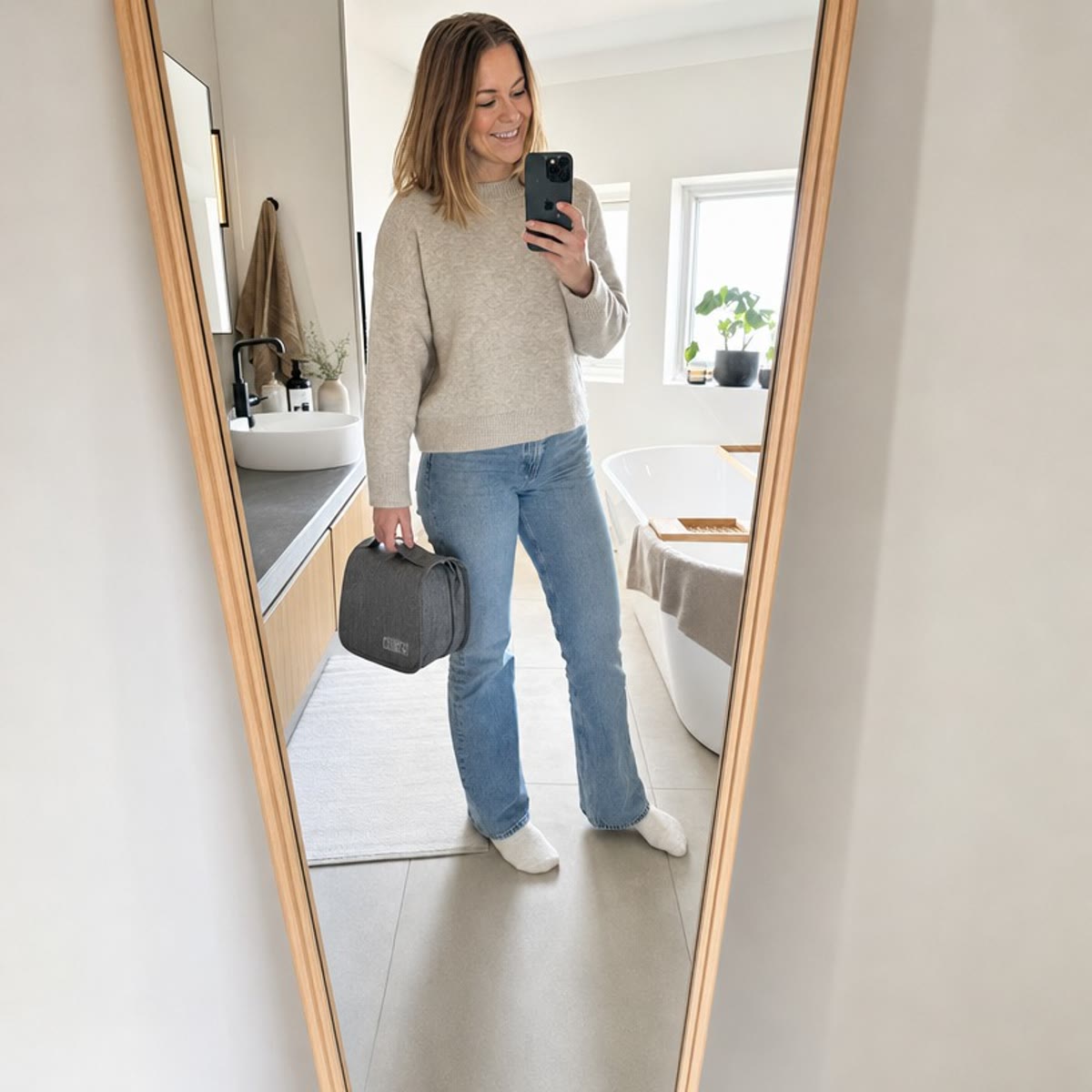 Vrouw die een spiegelfoto maakt met de grijze toilettas in haar hand